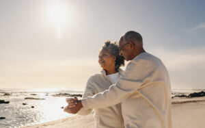 Older African American couple on the shore of a peaceful beach dancing together and enjoying the afternoon. They are enjoying retirement which includes a FERS Annuity Supplement.